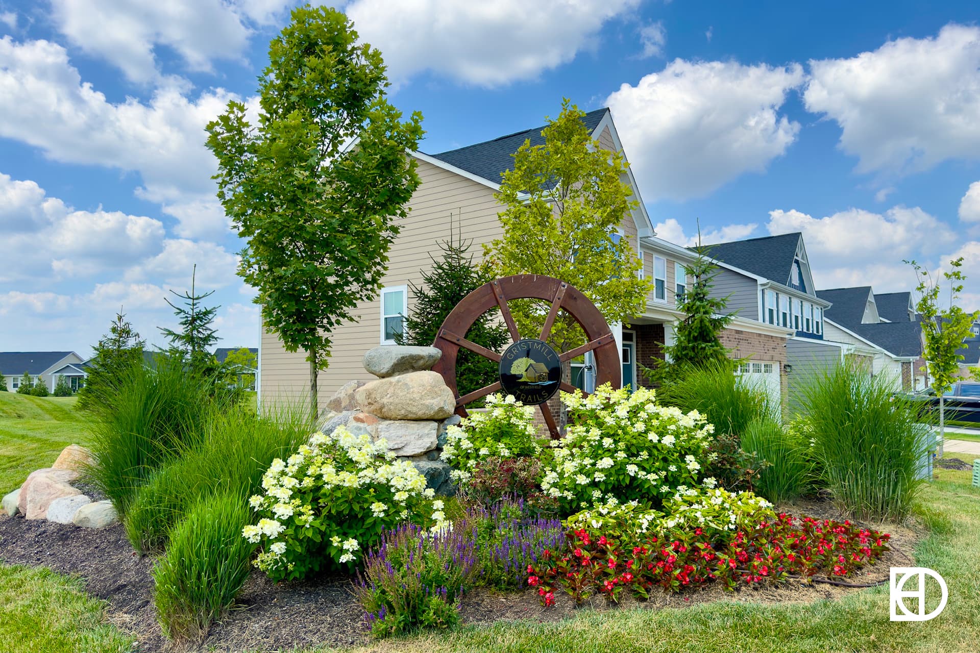 Photo of Gristmill Trails entrance with rocks, wagon wheel, landscaping and trees.