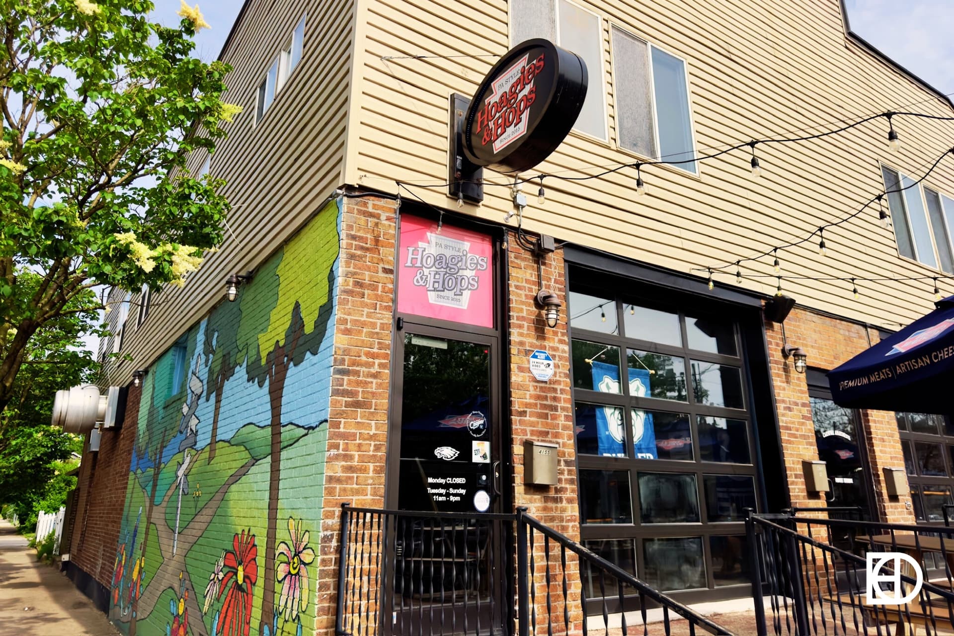 Exterior photo of Hoagies & Hops, showing patio, entrance, and mural 