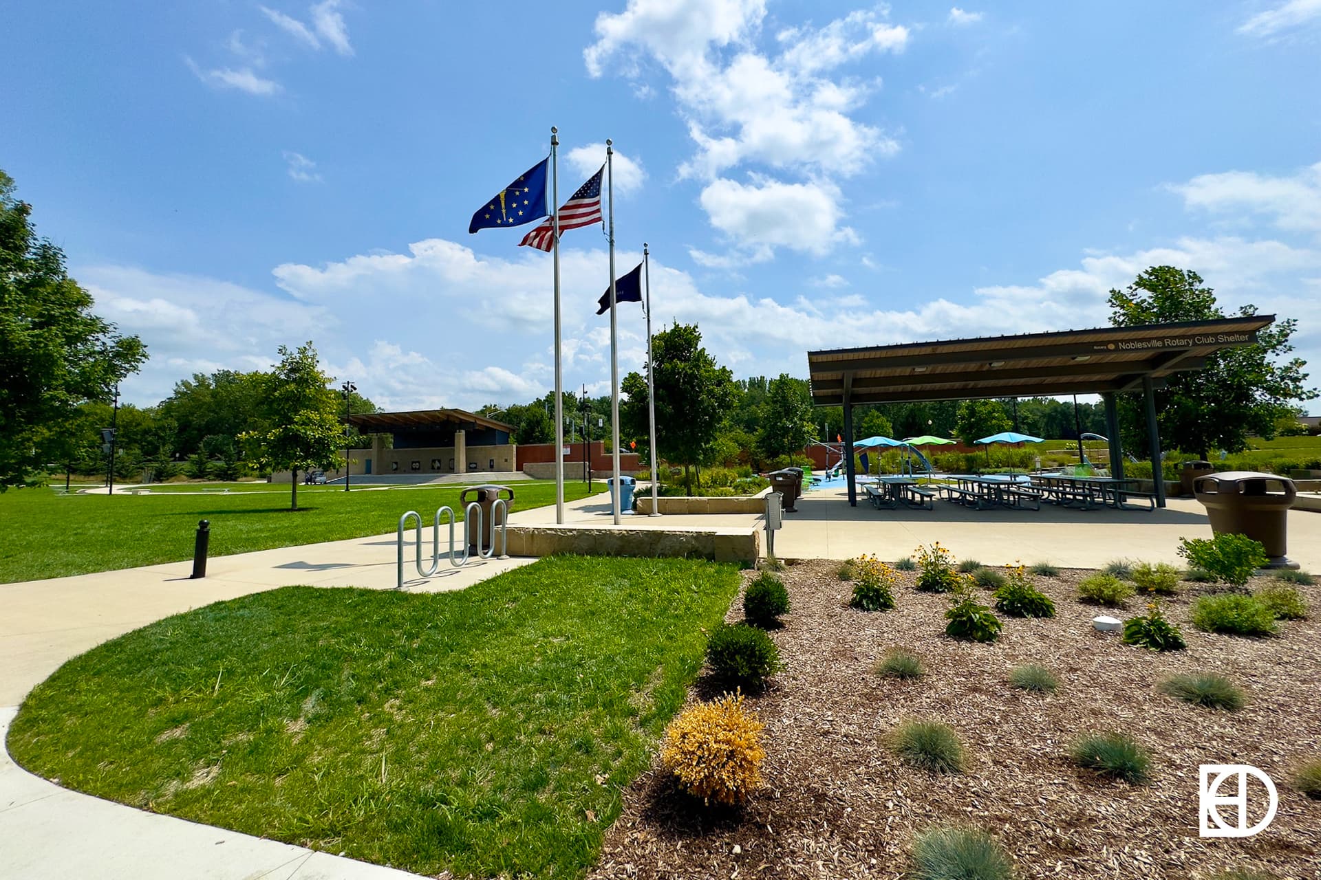 Photo of pavilion and flag poles with flags flying in front blue skies at Federal Hill Commons in Noblesville.