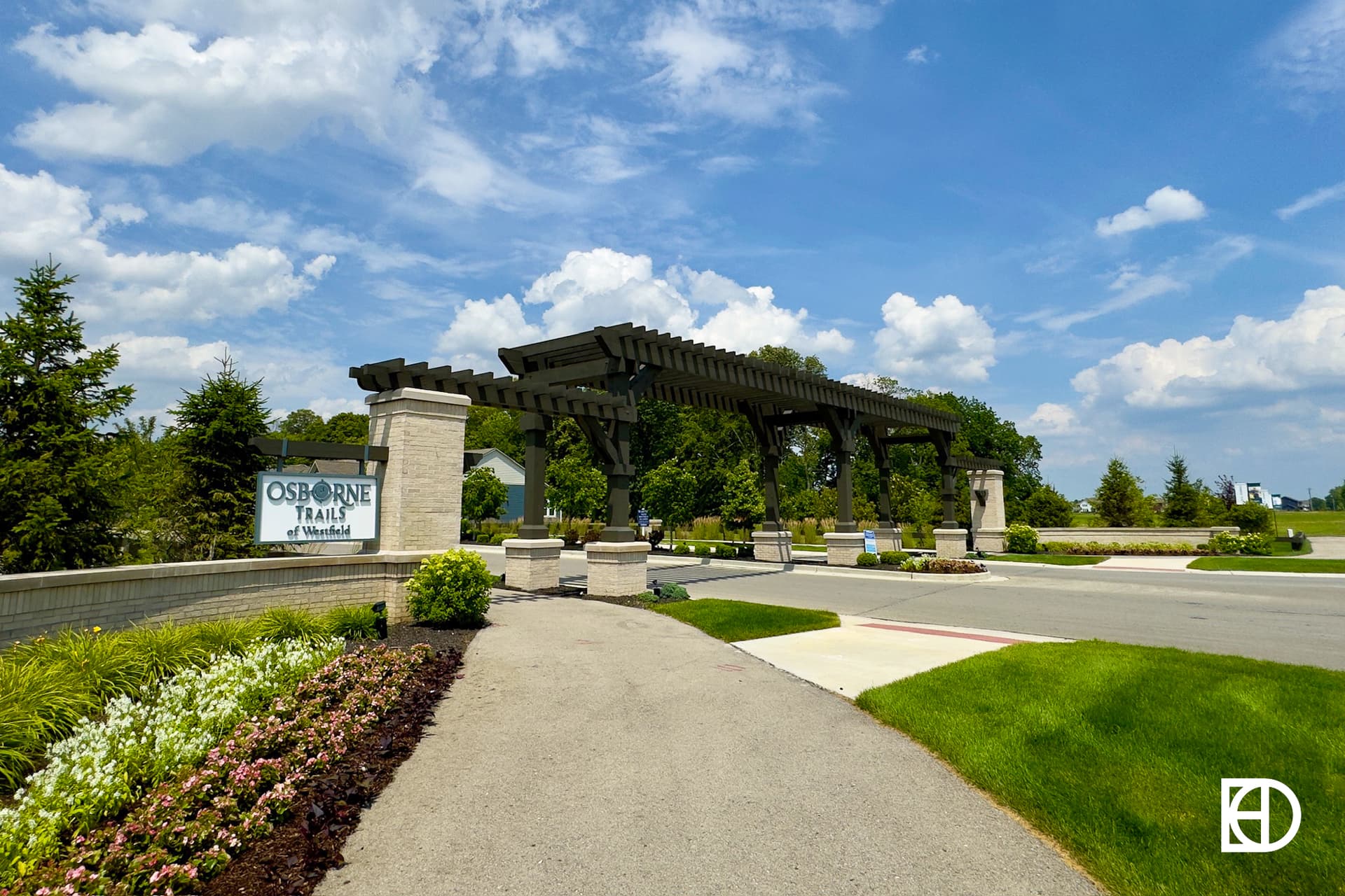 Photo of sidewalk and drive entering Osborne Trails with entrance sign and landscaping.