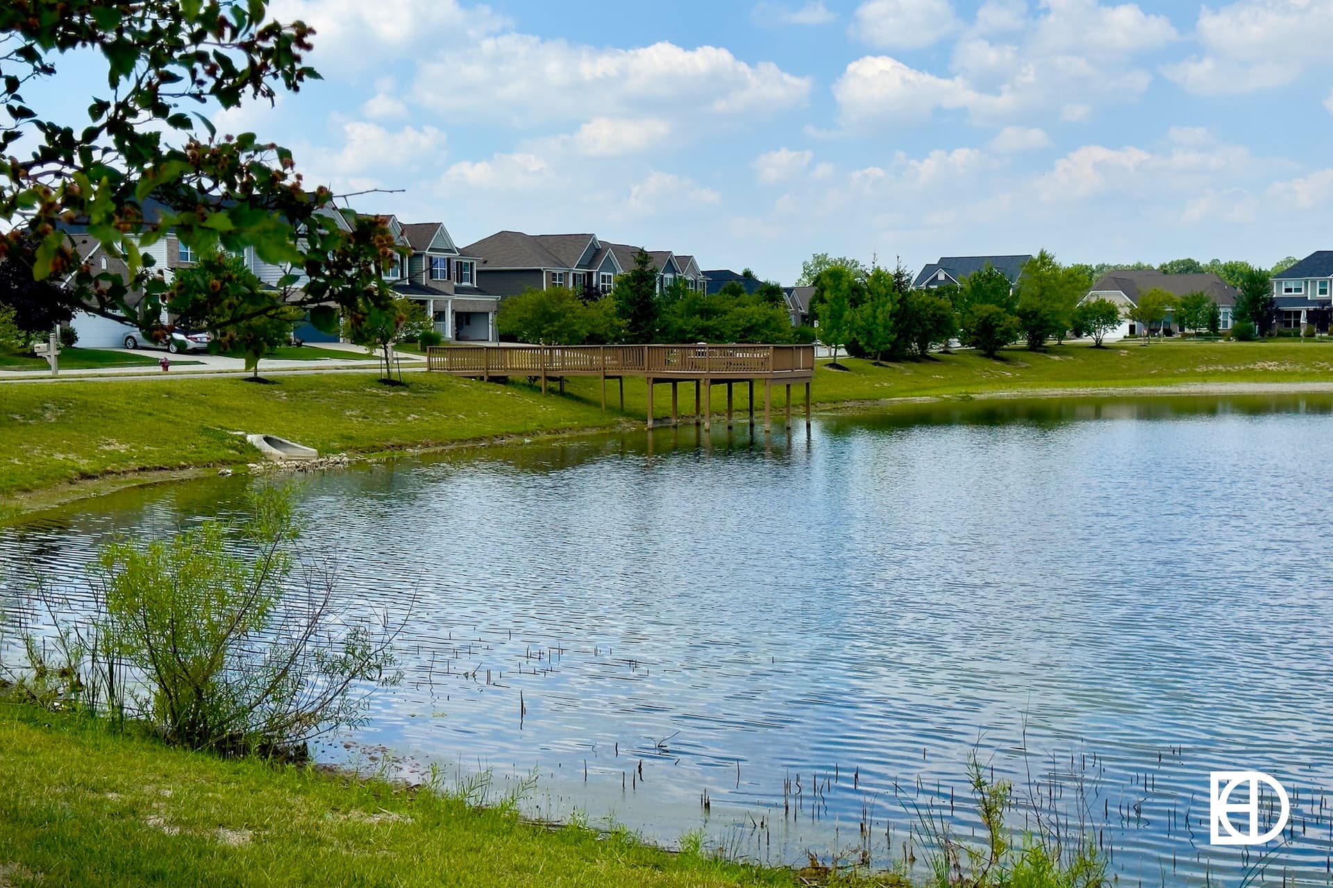 Pond at Waters Edge at Springmill Trails with homes in the background and large wood pier overlooking water.